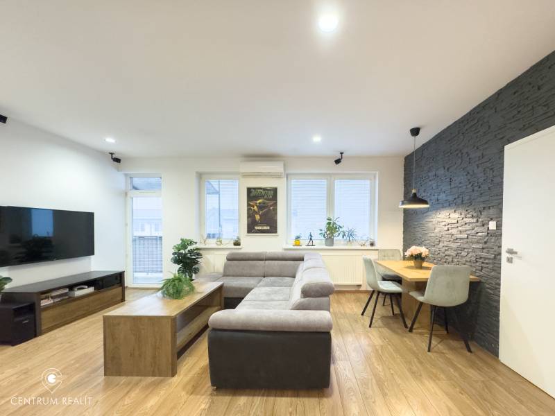 Living room in a 3-room apartment with wood-patterned flooring, a gray sofa, and a dining area.