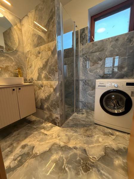 A bathroom with a washing machine, shower cabin, and marble tiles in a family house.