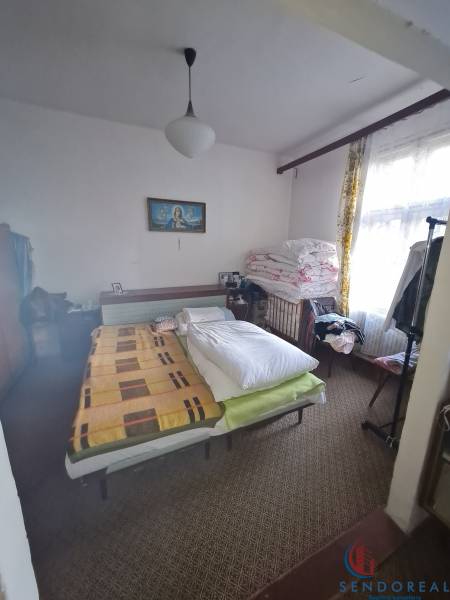 Bedroom in a family house with a colorful blanket, carpeted floor, and a picture on the wall.