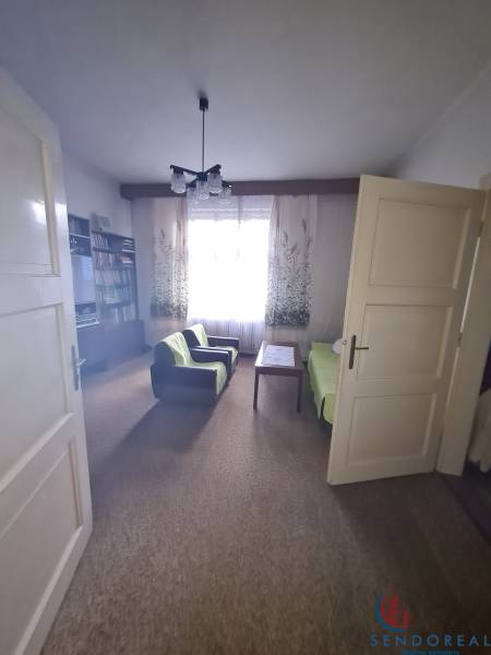 Living room in a family house with armchairs, a table, and a bookshelf, curtains letting in light.