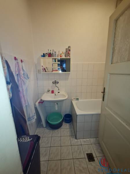 A bathroom in a family house with a bathtub, a sink, and a mirror, with tiles and white wall tiles.