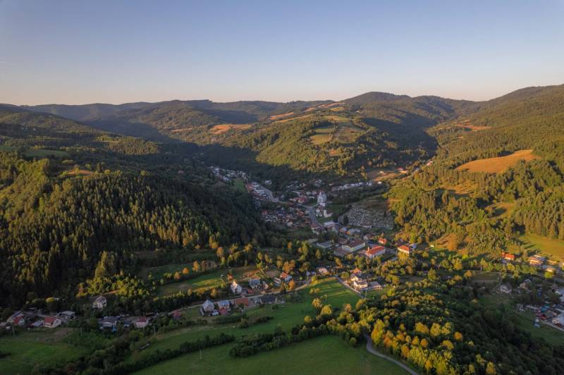 A mountainous landscape with agricultural and forest lands in the village of Lazy pod Makytou at sunset.