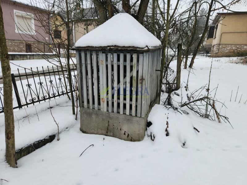 A snow-covered plot of land near a family house in Felsőtelekes with a metal shelter and trees.
