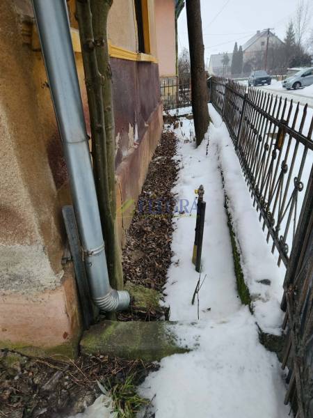 A snowy exterior of a family house in Felsőtelekes, next to the gutter pipe and fence.