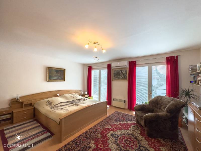 Bedroom in a family house with a double bed, an armchair, and balcony doors, floor with wooden decor.