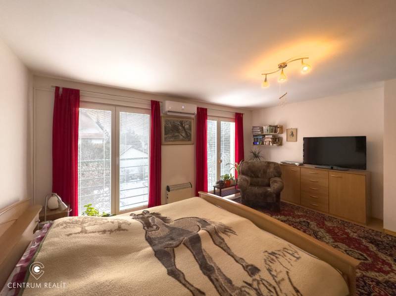 A bedroom in a family house with access to a balcony, red curtains, and a comfortable armchair.