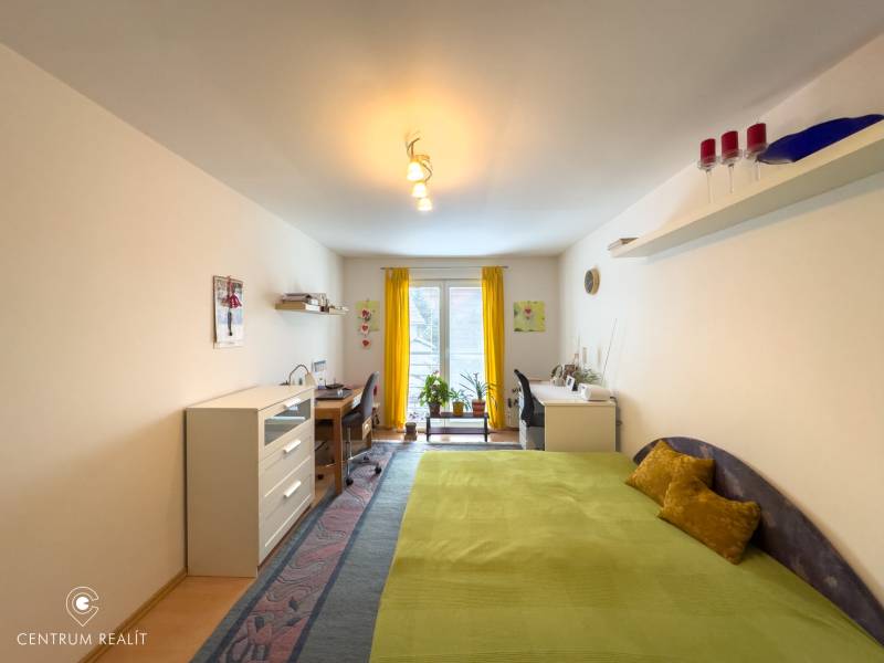 A room with a bed, a desk, a yellow curtain, and a floor with a wooden decor in a family house.