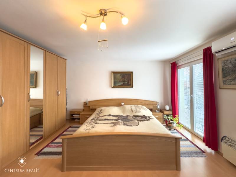A bedroom in a family house with a wood-patterned floor, a large wardrobe, and balcony doors.