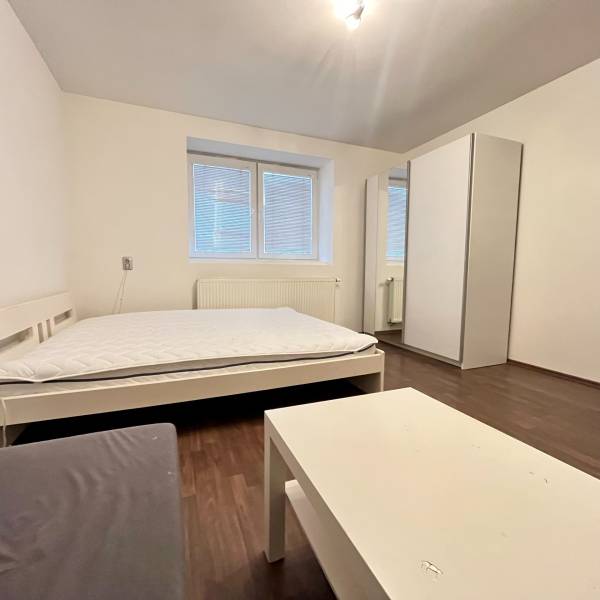 White bed, wardrobe, table, and floor with wood decor in a studio apartment.