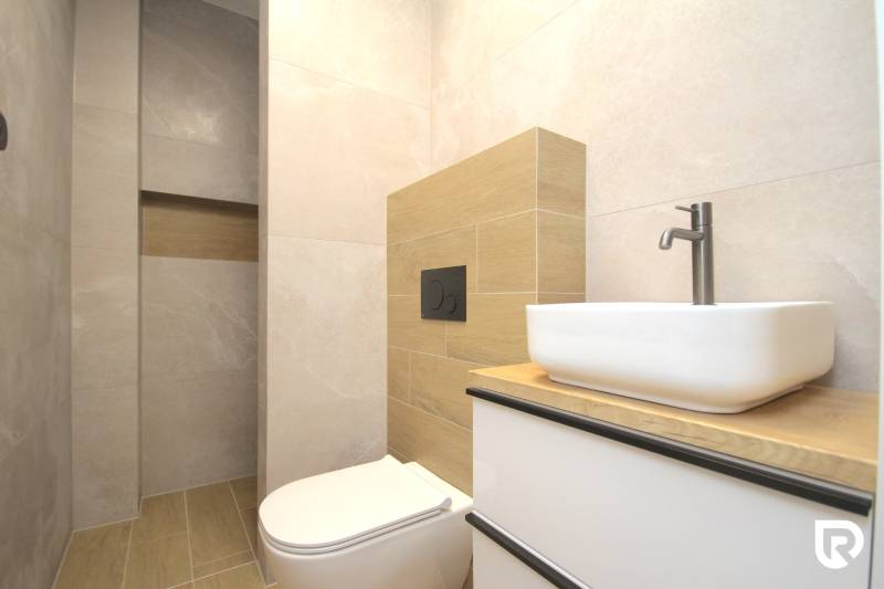 Bathroom in a family house with a sink, toilet, and tiles with a wooden decor.