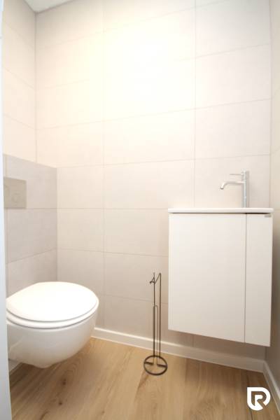 A toilet in a family house with a wooden decor floor and white walls.