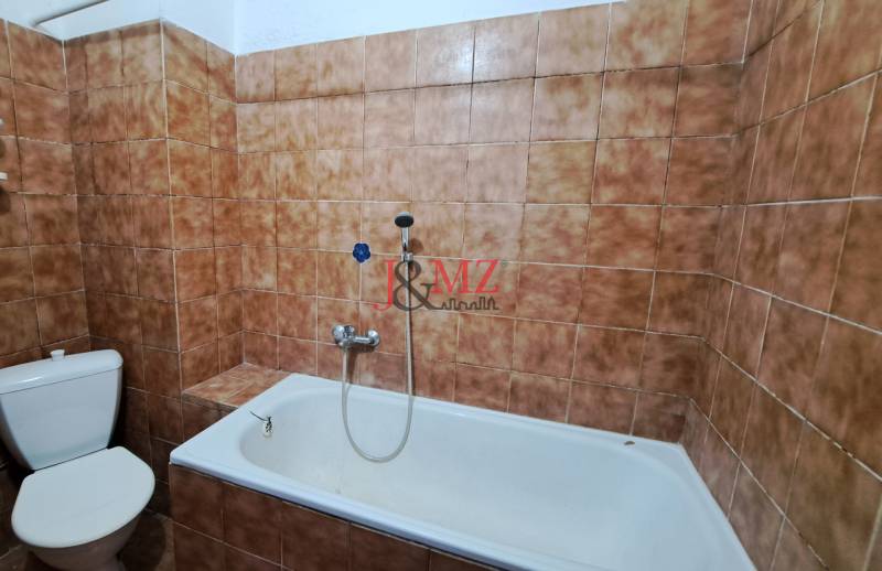 Bathroom in a family house, tiled with brown tiles, with a bathtub and a toilet.
