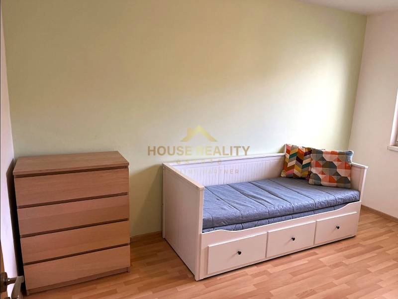 A bright room in a 3-room apartment with a bed and a dresser on a wooden-decor floor.