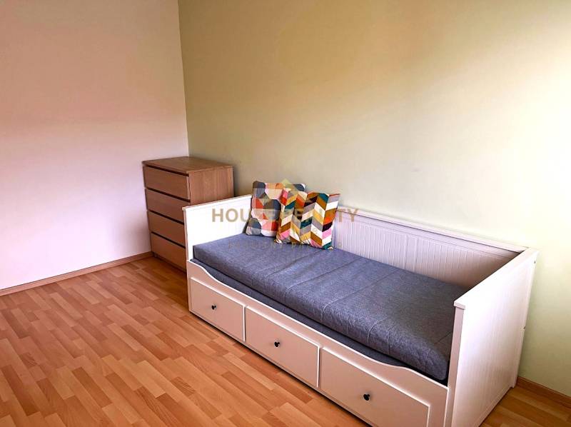 A room in a 3-room apartment with a sofa, drawers, and a floor with a wood decor.