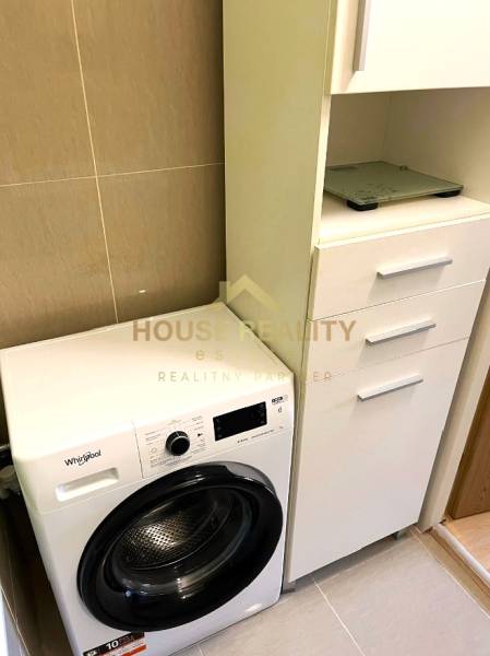 A bathroom in a 3-room apartment with a washing machine and white cabinets for storage.