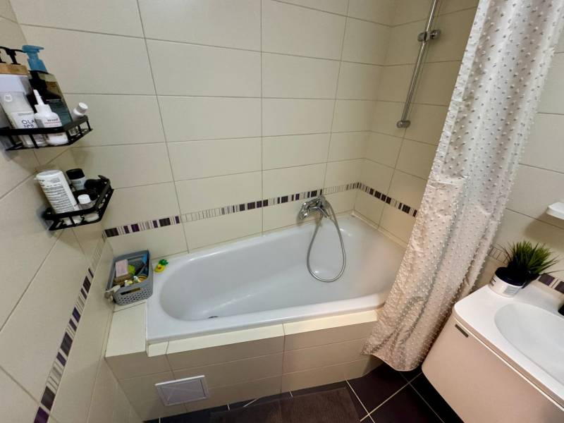 Bathroom in a 3-room apartment with a bathtub, shower screen, and accessories on the shelves.