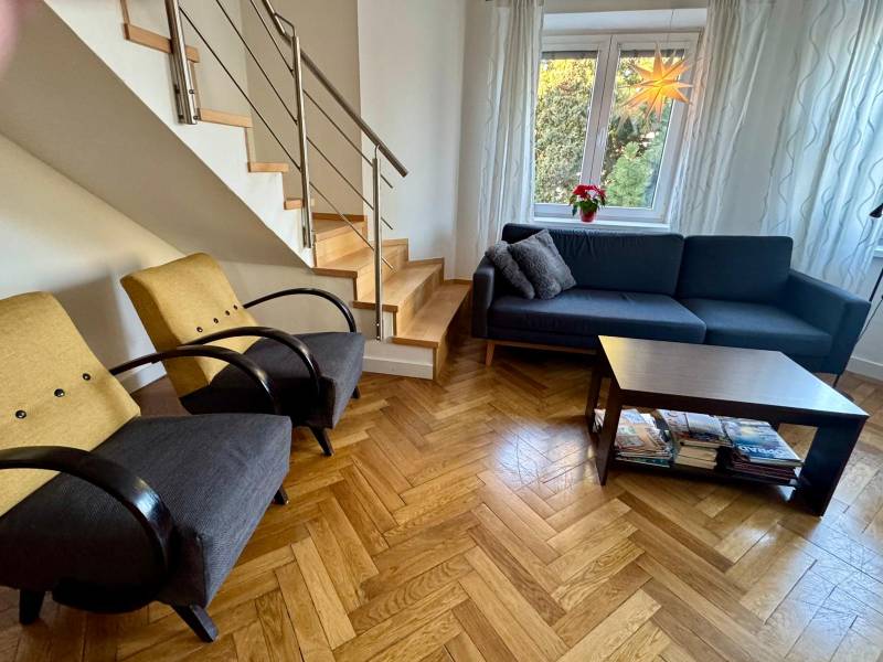 Living room in a 3-room apartment with a wooden decor floor, staircase, sofa, and armchairs.