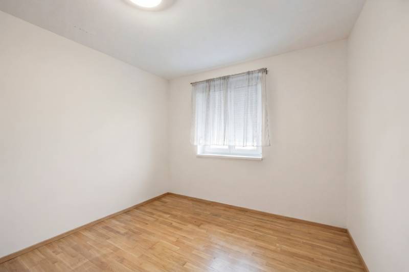 A room with a window, a white wall, and a wooden decor floor in a family house.