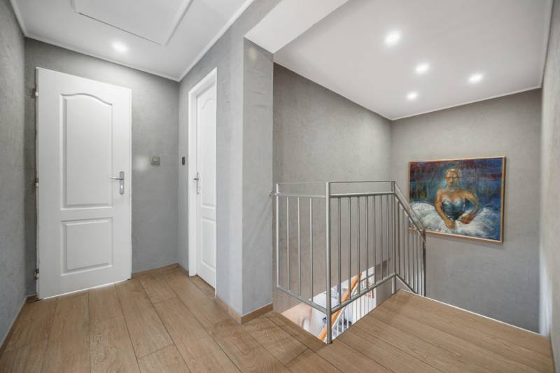 A hallway in a family house with a wooden decor floor, a painting, and a railing.