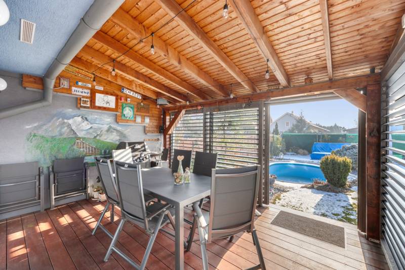 Terrace of a family house with a wooden ceiling, table, and view of the pool.