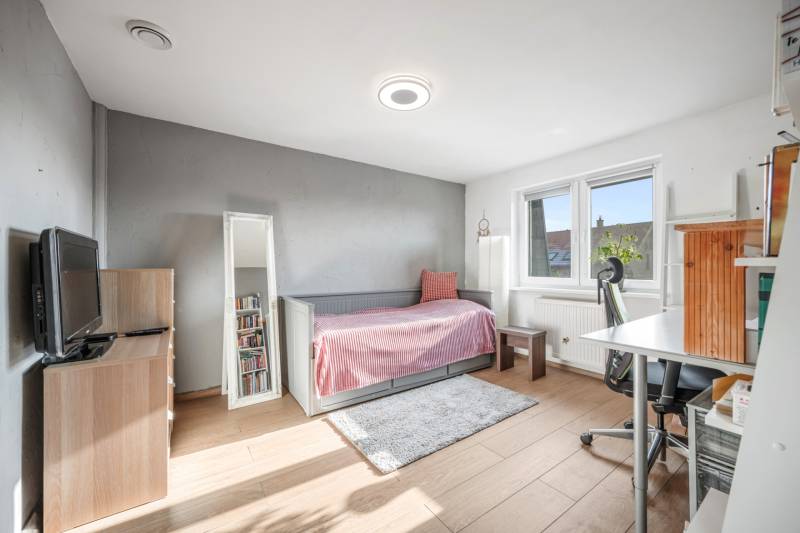 A bright room with a bed, a desk, a mirror, and a wooden floor in a family house.