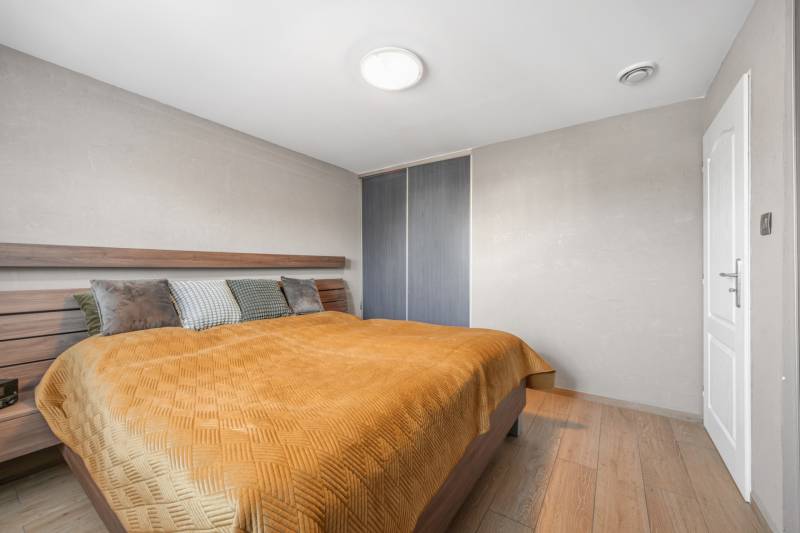 Bedroom in a family house with a bed, wardrobe, and wooden decor flooring.