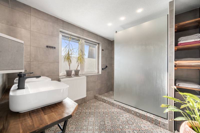 A bathroom in a family house with ceramic tiles, a sink, and a glass shower screen.