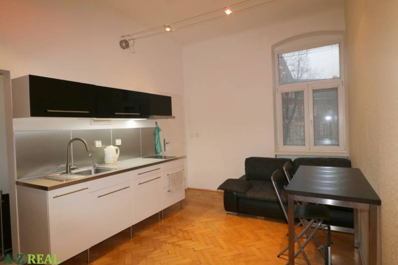A kitchen in a 3-room apartment with a wooden decor floor and black furniture.