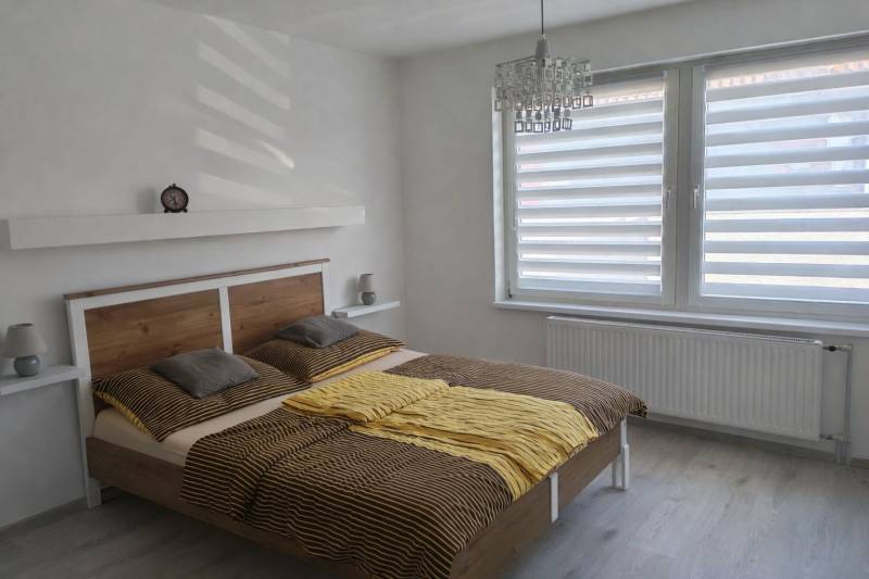 Bright bedroom with a large window, bed, and wood-patterned floor in a family house.