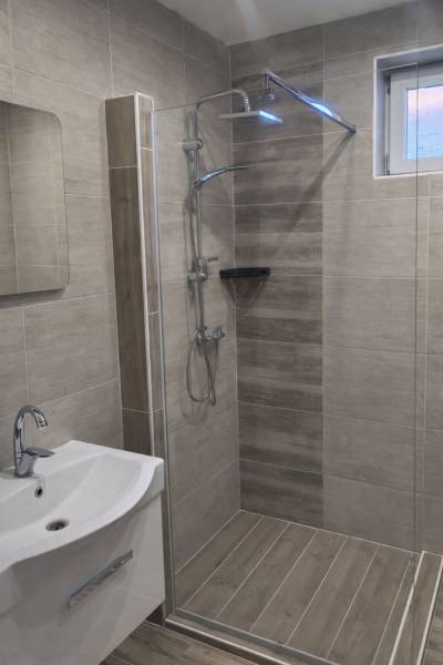 A shower corner in a family house with a wooden decor floor and a sink.
