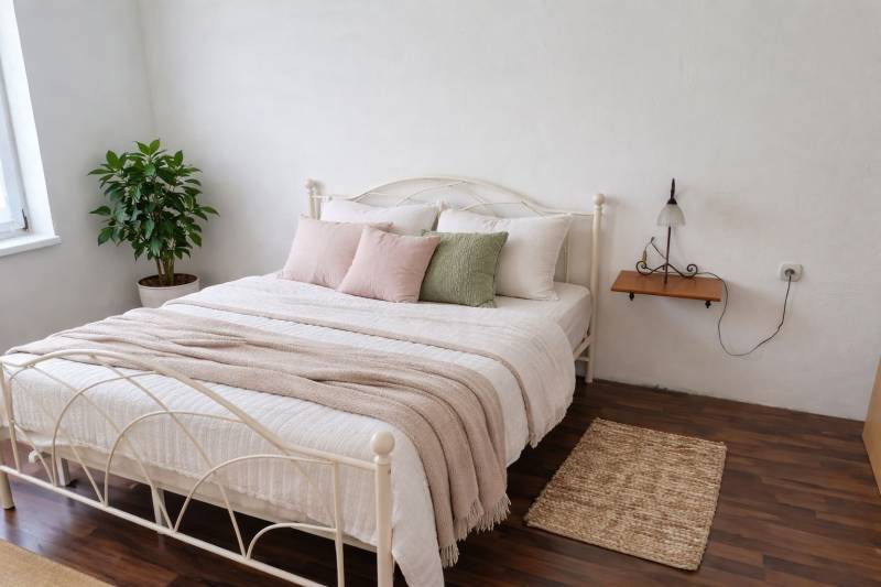 Bedroom in a family house with a bed, decorative pillows, and a wooden-patterned floor.