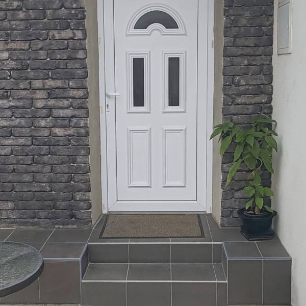 Entrance to a family house in Horné Saliby, white door, brick cladding, stairs with greenery.