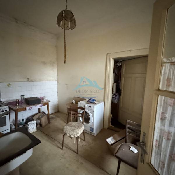 A kitchen in a family house with older furnishings, a washing machine, and wooden furniture.