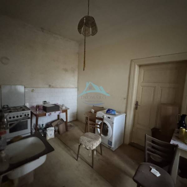 A kitchen in a family house with a sink, stove, and washing machine, with old furniture and lighting.