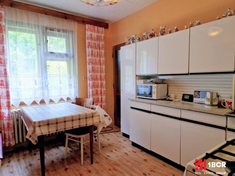 A kitchen in a family house with a wooden decor floor, white cabinets, and a checkered tablecloth.