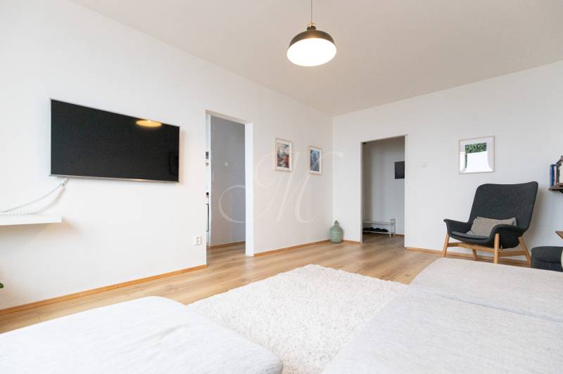 Living room in a three-room apartment with a television, sofa, and wooden decor flooring.