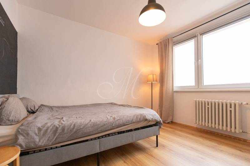 Bedroom in a 3-room apartment with a comfortable bed, wood-patterned flooring, and a large window.