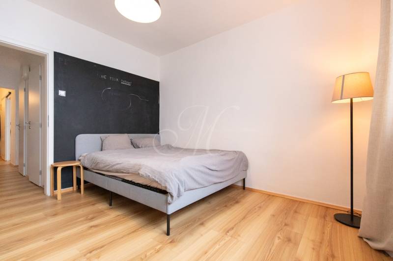 A bedroom with a bed, wood-patterned flooring, and a standing lamp in a three-room apartment.