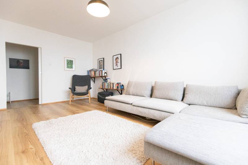 Living room in a three-room apartment with a wooden decor floor, gray sofa, and books.