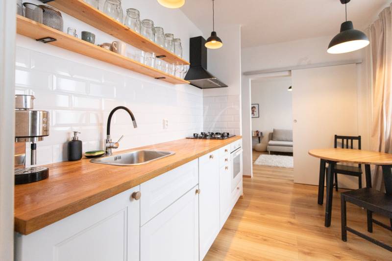 A kitchen in a 3-room apartment with white cabinets, a dining table, and a floor with a wood decor.