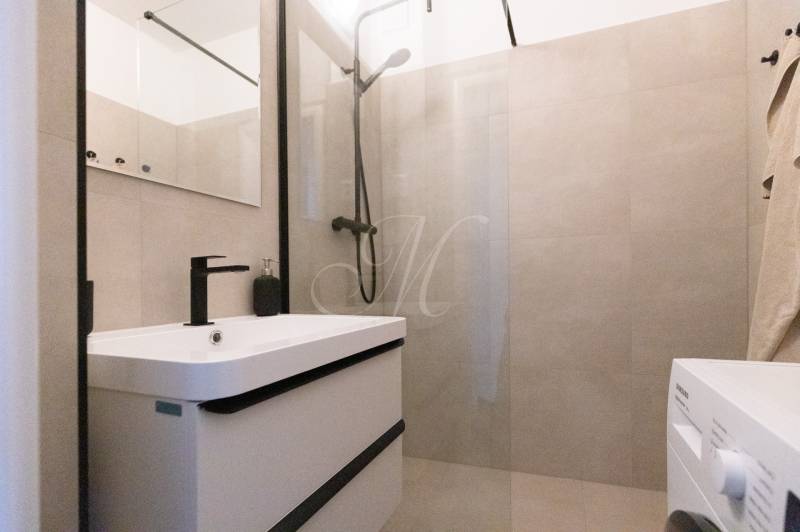 A bathroom in a 3-room apartment with a bathtub, black faucet, and washing machine.