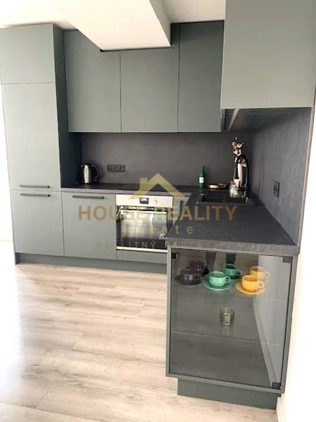 A kitchen in a 3-room apartment with a wood-patterned floor and gray cabinets.