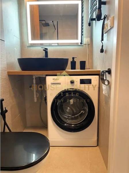 Compact bathroom with a washing machine and wooden decor flooring in a 3-room apartment.