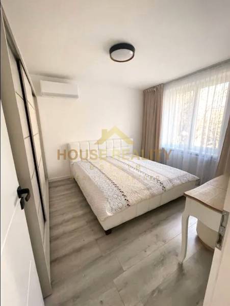 Bedroom in a 3-room apartment with a large window, bed, and wooden decor flooring.