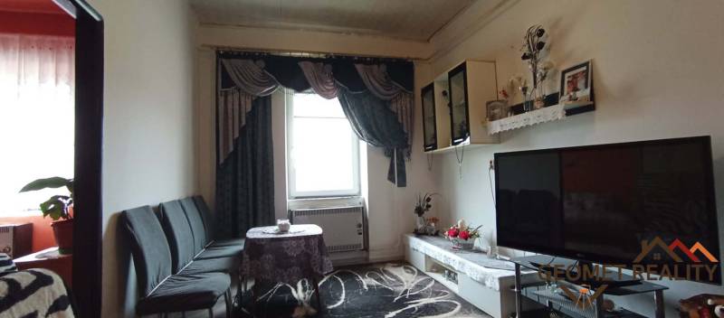 Living room in a two-room apartment with a television, sofa, and decorative curtains.
