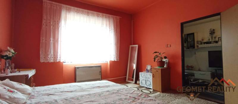 A bedroom in a two-room apartment with bright orange walls and a carpet.