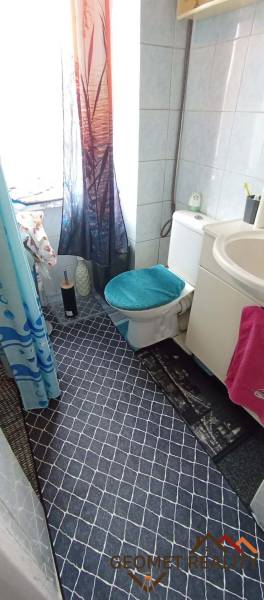 Bathroom in a 2-room apartment with white tiles and patterned floor.