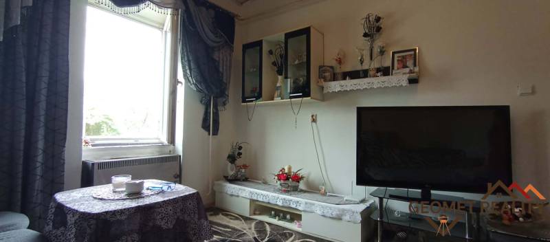 Living room in a two-room apartment with a table, television, and decorations on the shelves.