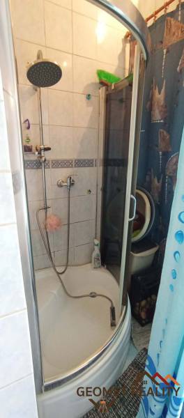 Bathroom in a 2-room apartment with a corner shower and tiles.