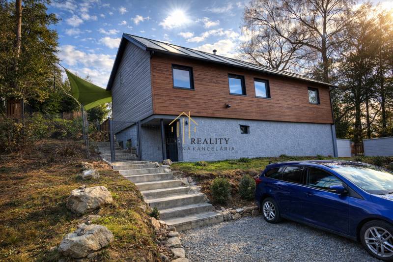 A cottage in Zvolen with wooden cladding, stairs, and a parked car on a gravel surface.